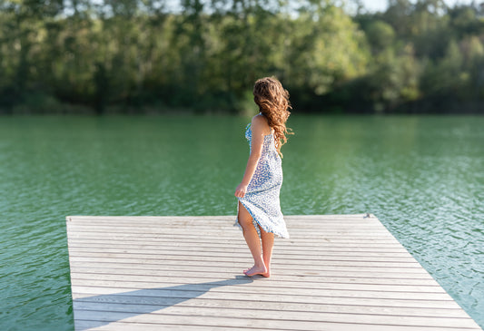 High School Senior girl in blue floral dress standing on a lake dock, capturing a serene moment with a natural lake backdrop.